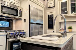 A modern kitchen with stainless steel appliances, a built-in oven, a microwave, a double-door refrigerator, and a sink with a faucet.
