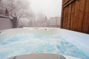 A hot tub with a wooden deck and a view of a snowy landscape.