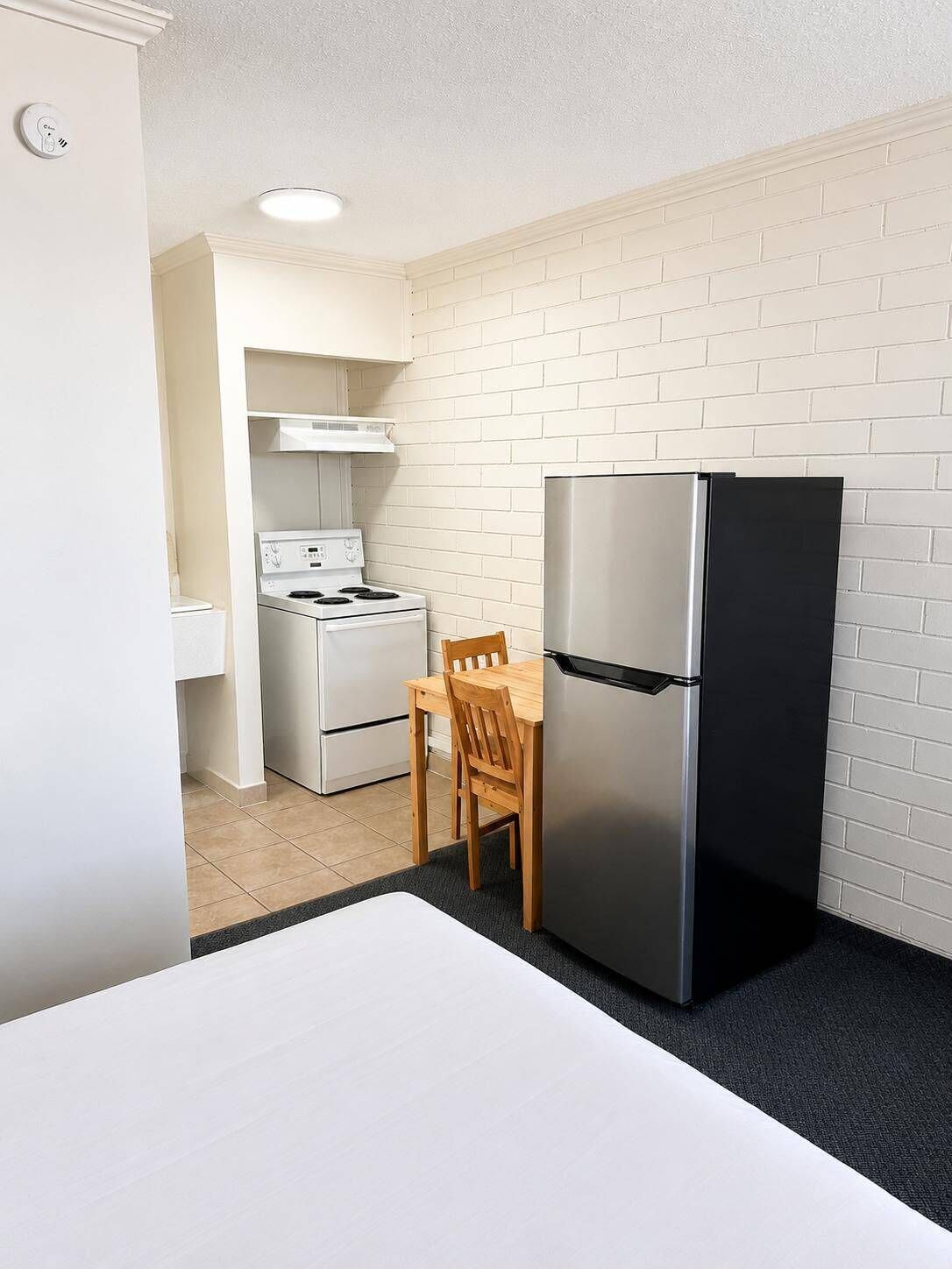 Una cocina funcional con estufa, refrigerador y una pequeña mesa de comedor con sillas.