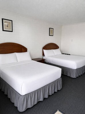 Een hotelkamer met twee eenpersoonsbedden, witte beddengoed, houten hoofdborden en een grijs vloerkleed.