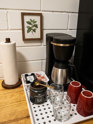 En kaffestation med en kaffebryggare, en burk med kaffe, en rulle hushållspapper och två röda muggar på ett bricka.