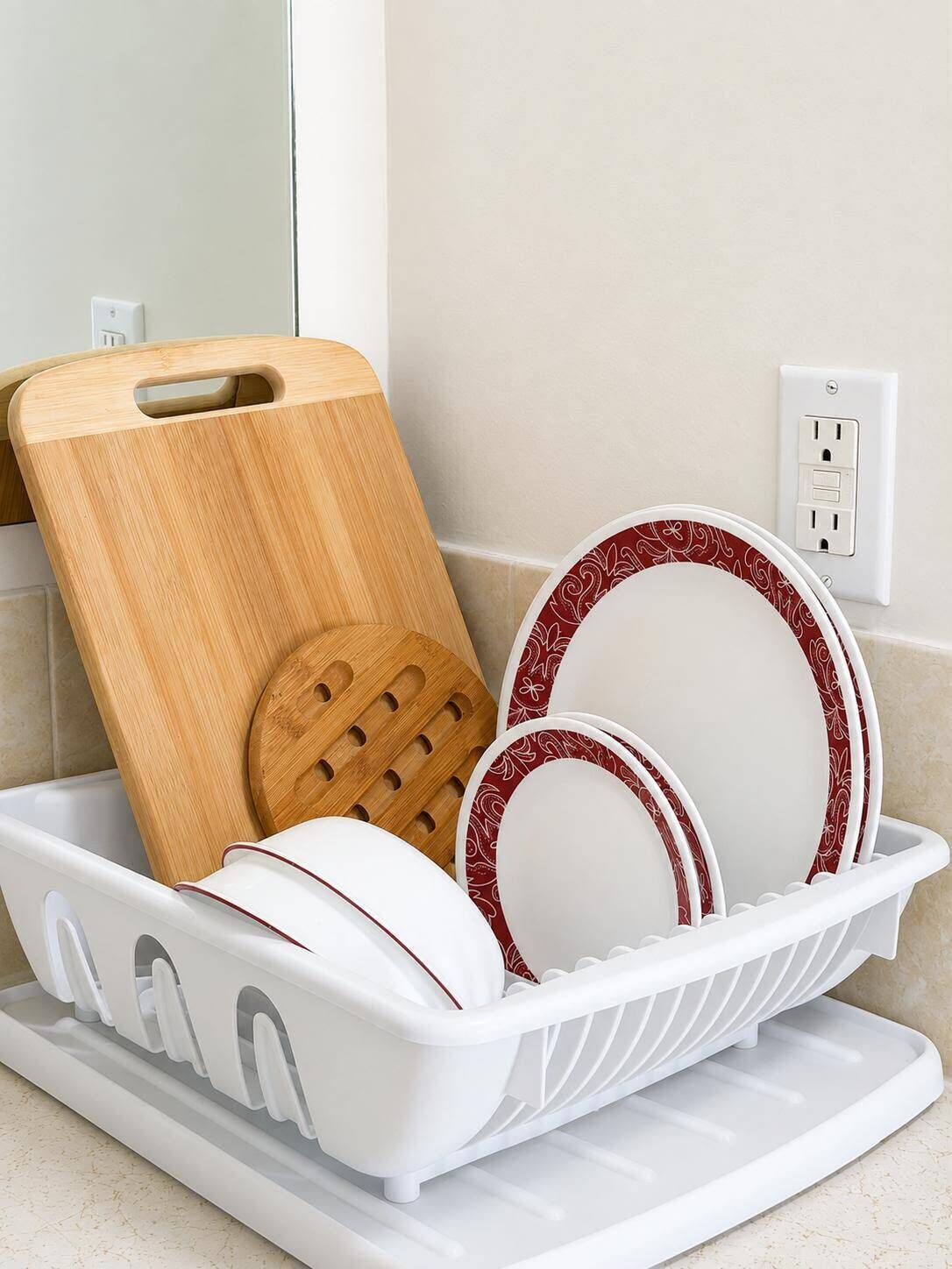 Un égouttoir à vaisselle blanc avec des assiettes et une planche à découper en bois.