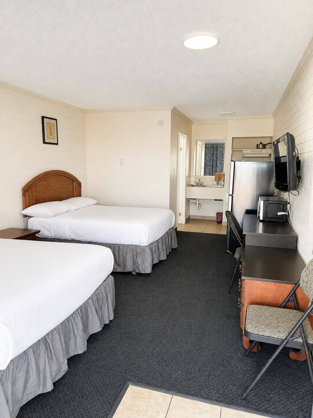 Une chambre d’hôtel avec deux lits simples, un petit bureau avec une chaise, une télévision et un coin cuisine.