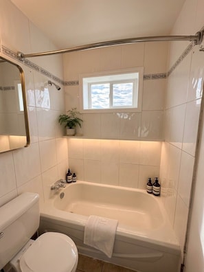 Un baño con bañera, inodoro y una ventana sobre la bañera.