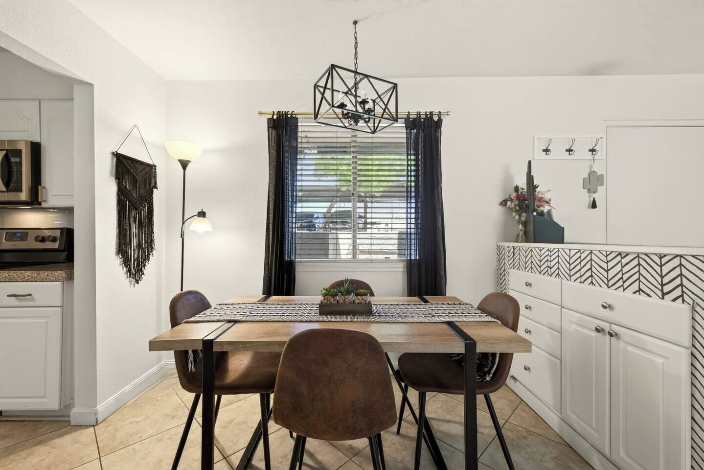 A modern kitchen with a dining table, chairs, a hanging light fixture, and a microwave.