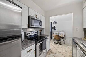 Eine Küche mit Kühlschrank, Mikrowelle, Herd, Backofen sowie ein Essbereich mit Stühlen und Tisch.