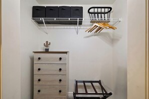 Ein Stauraum mit einer Holzkommode, einem Metallregal mit schwarzen Aufbewahrungsboxen und einem Metallgestell mit Holzkochlöffeln.