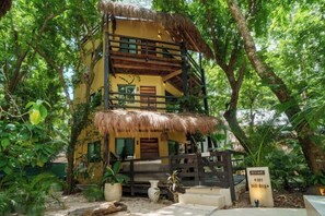 Un bâtiment à deux étages, doté d’un toit de chaume et entouré d’une végétation luxuriante.