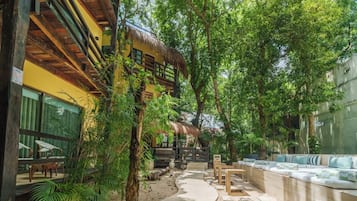 A hotel corridor with a thatched-roof structure, outdoor seating, and lush greenery.