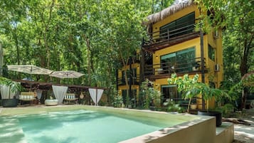 A two-story building with a pool, surrounded by lush greenery.