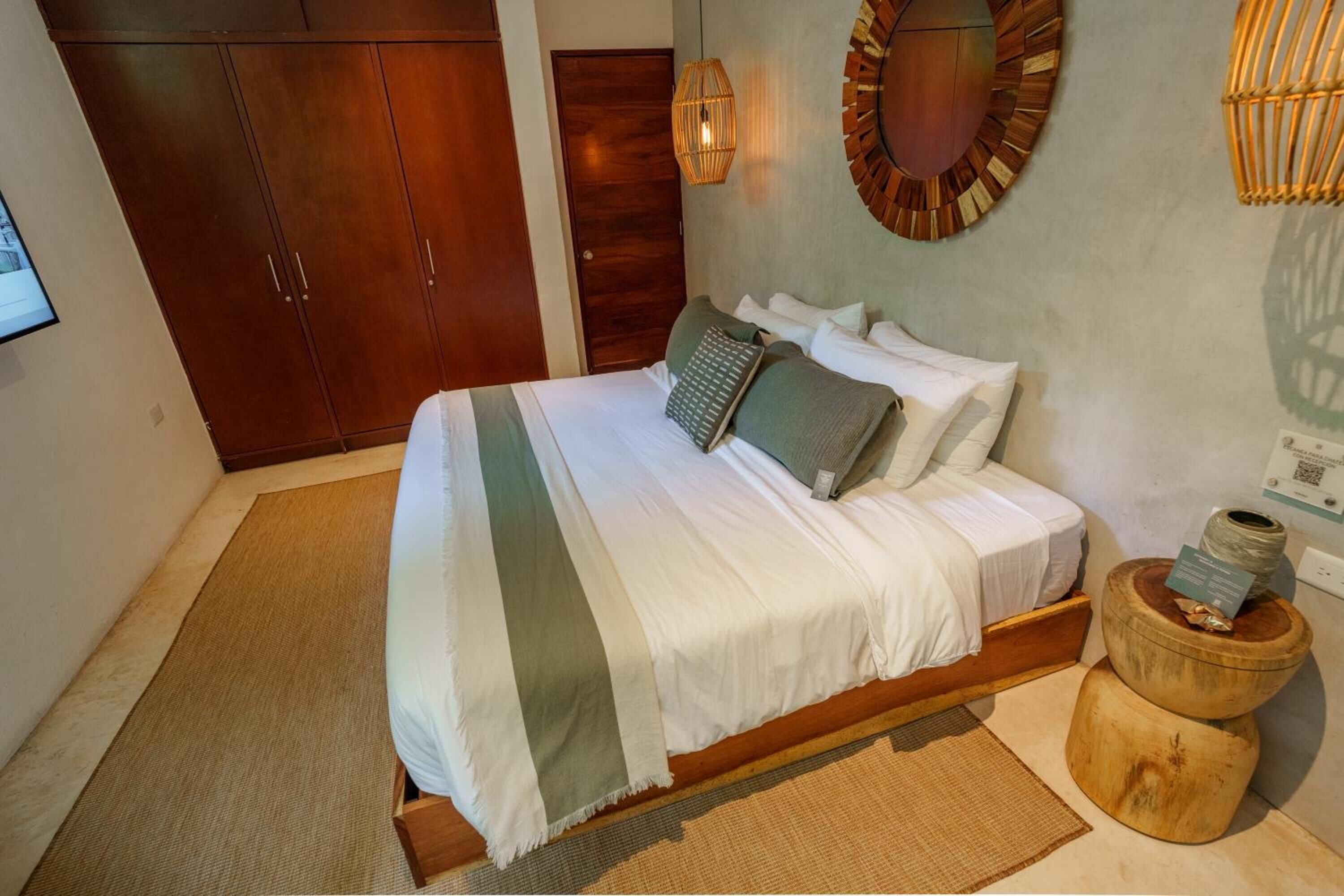 A bedroom with a bed, wooden wardrobe, wall-mounted lamp, and a round mirror.