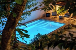 Een binnenzwembad met een heldere blauwe waterpartij, omgeven door weelderige beplanting en modern tuinmeubilair.