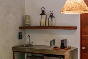 Een keuken met een houten aanrecht, een gootsteen, een kraan, een hangende lamp en een plank met kaarsen.