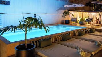 A poolside lounge area with a long bench, potted plants, and a small table.