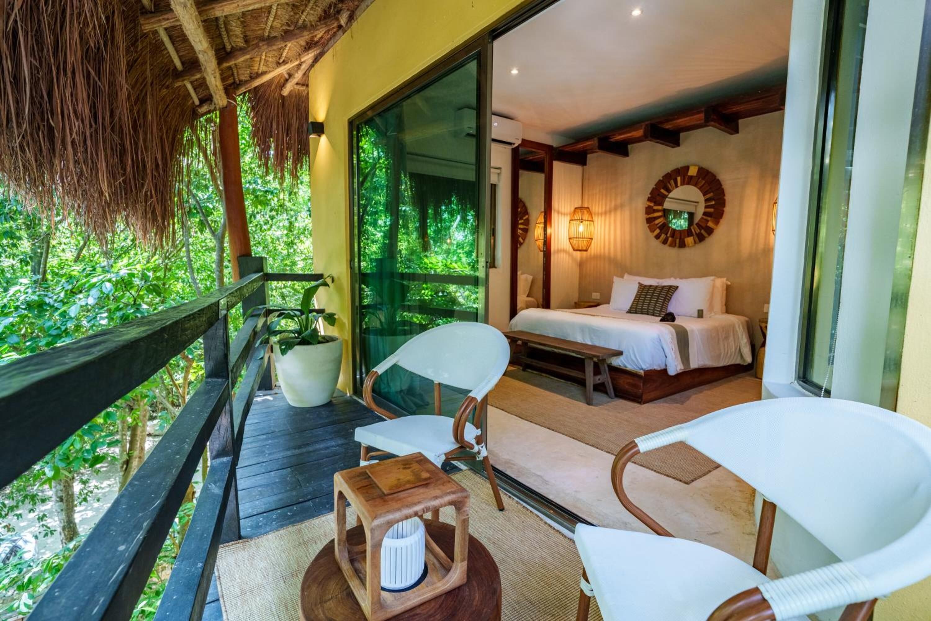 A room with a bed, two chairs, a small table, and a potted plant.