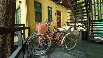 A bicycle parked on a wooden deck with a basket attached, near a building with a yellow exterior and a wooden fence.