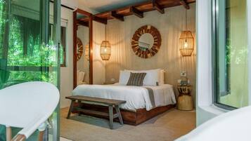 A bedroom with a large bed, bedside tables, a bench, and a view of greenery through a window.