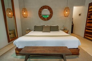 Un dormitorio con una cama grande, dos mesitas de noche, un banco de madera, un espejo redondo y dos lámparas de pared.
