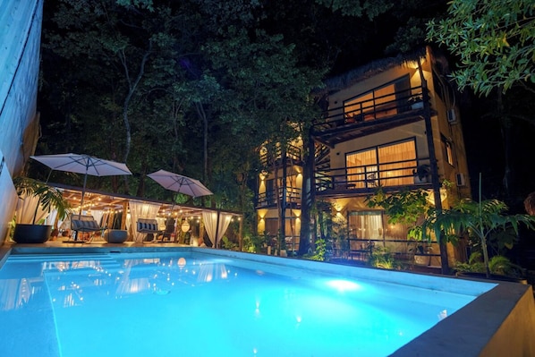 Un bâtiment moderne doté d’une piscine, entouré d’arbres et offrant des espaces de détente en plein air.