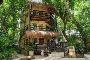Un bâtiment à deux étages, doté d’un toit de chaume et entouré d’une végétation luxuriante.
