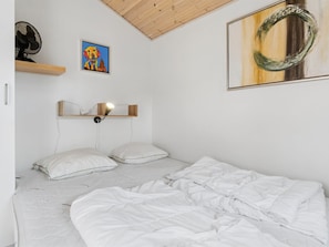 A bedroom with a bed, two pillows, a bedside table with a lamp, a wall-mounted shelf, a fan, and two artworks. - "Sannie" - 2.8km from the sea by Interhome (Gudhjem)