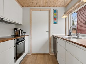 Eine kleine Küche mit Holzboden, weißen Schränken, einem Edelstahlbackofen und einem Geschirrspüler.