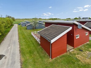 A row of red buildings with satellite dishes, a paved road, and green fields in the background. - "Sannie" - 2.8km from the sea by Interhome (Gudhjem)