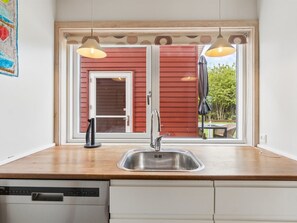 A kitchen with a stainless steel sink, a dishwasher, and a window with a view of a red building and greenery outside. - "Sannie" - 2.8km from the sea by Interhome (Gudhjem)
