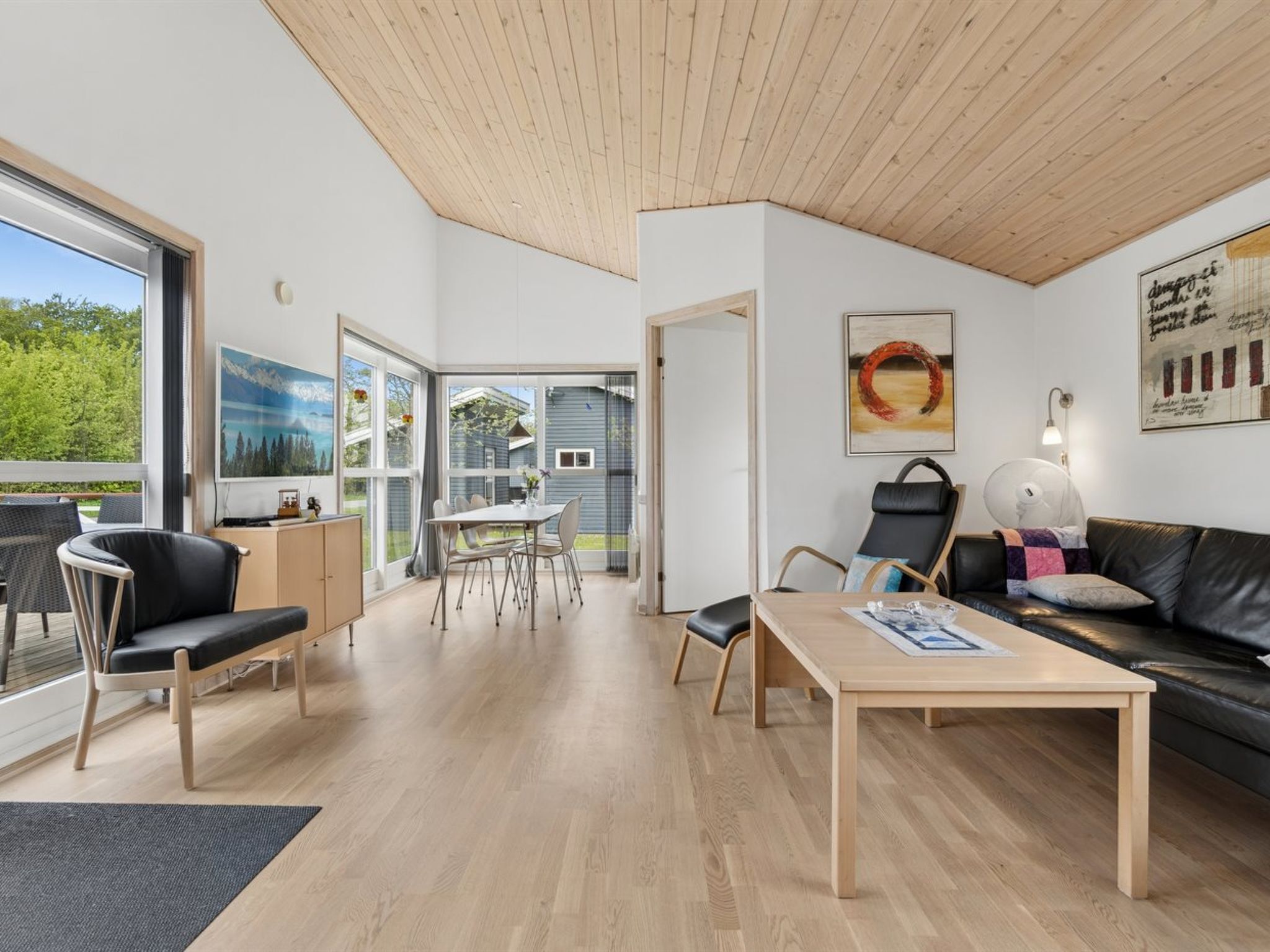 A modern interior with a dining area, a sofa, and a view through a glass door.