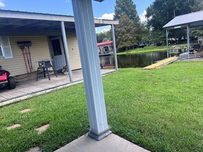 A residential property with a covered patio, a lawn, a dock extending into a lake, and a red vehicle parked outside.