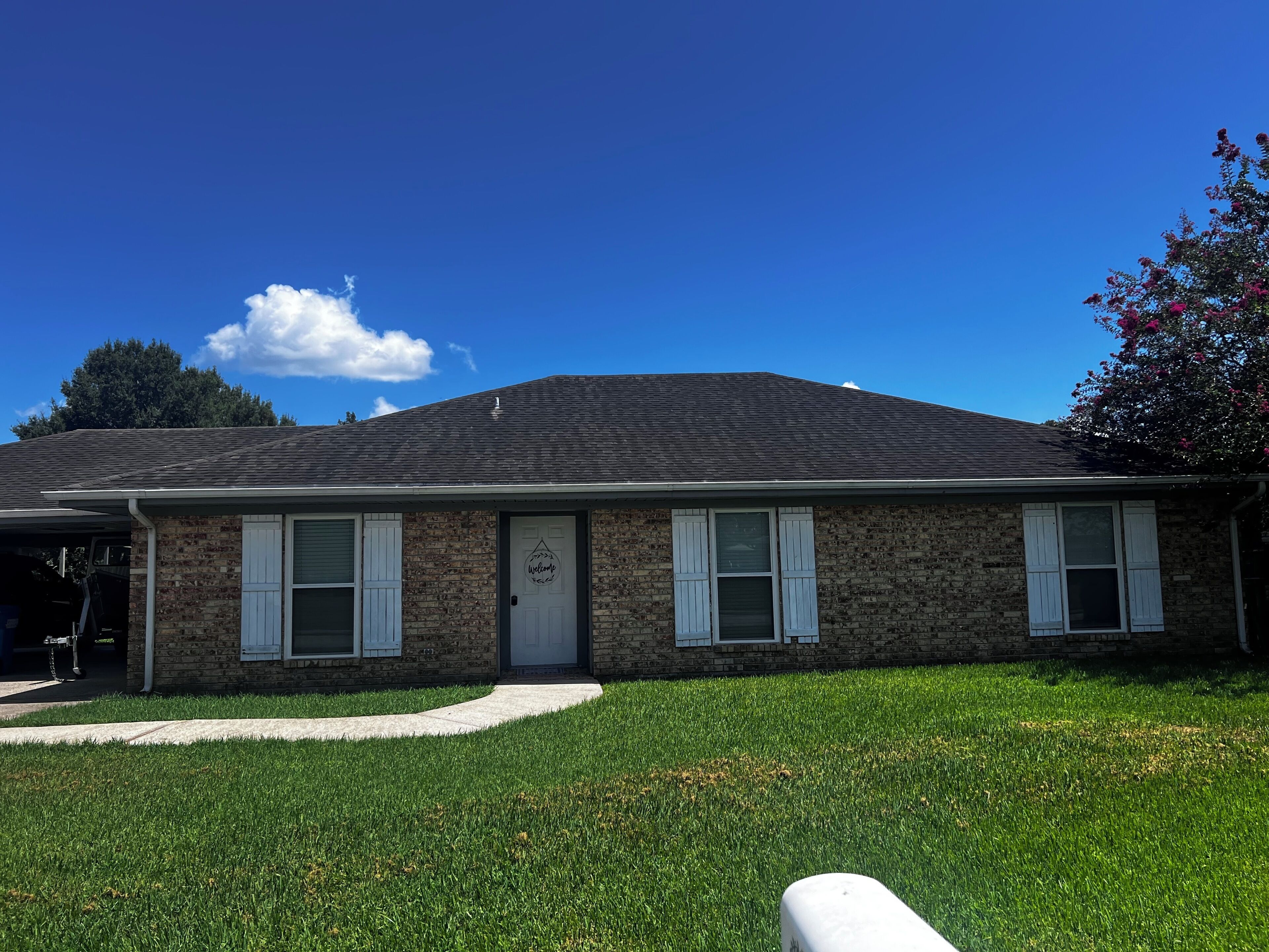 Une maison à deux étages, construite en briques, avec un porche à l’avant, un garage et une pelouse bien entretenue.