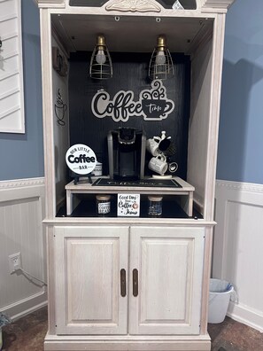 A coffee station with a coffee maker, mugs, and a sign that reads 'Good Day Start with Coffee & Jesus.'