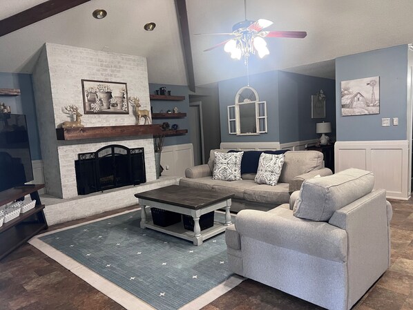 A living room with a fireplace, a ceiling fan, and a blue wall.