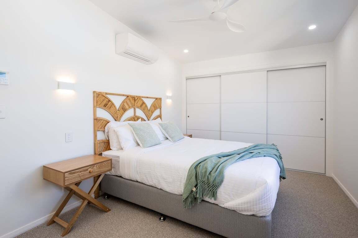 A bedroom with a bed, bedside table, wall-mounted light, ceiling fan, and a closet.