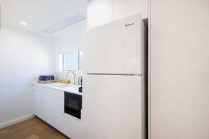 A compact kitchen with a white refrigerator, a built-in oven, and a sink. - Aqua - Front row living on Woolgoolga Beach (Woolgoolga)