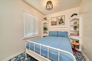 A bedroom with a bed, a window with blinds, a wall-mounted shelf with plants, and a ceiling light fixture. - Cozy 2BR Long Beach Retreat (Long Beach)