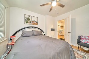 A bedroom with a bed, a ceiling fan, a nightstand, a lamp, and a door leading to a kitchen. - Cozy 2BR Long Beach Retreat (Long Beach)