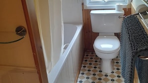 Une petite salle de bain comprenant des toilettes, une baignoire et une fenêtre avec des stores.
