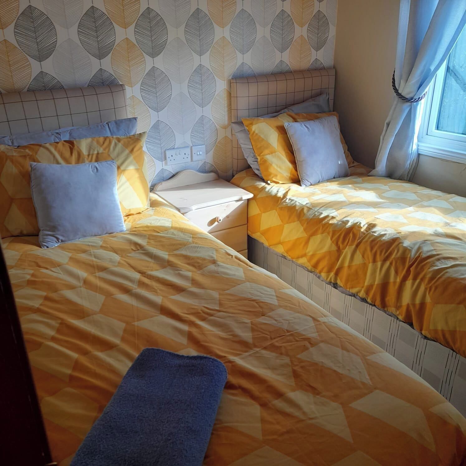 Una stanza con due letti, ognuno con una coperta a motivi e un comodino, e una parete decorata con un motivo a foglia.