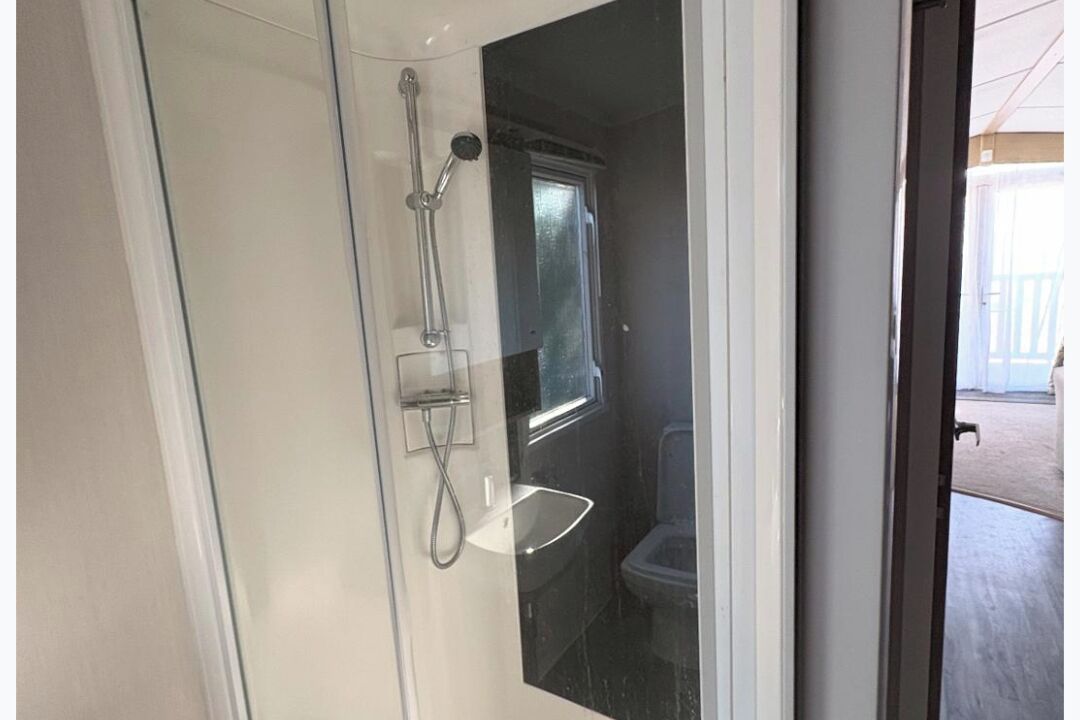 A glass-enclosed shower area with a handheld showerhead and a wall-mounted faucet.