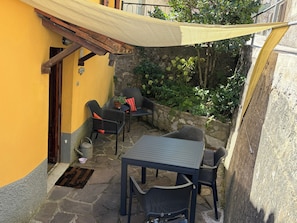 An outdoor patio with stone flooring, a table, chairs, and a yellow wall. - House - Sleeps 6 - Garden, Parking, Pet Friendly (Molazzana)