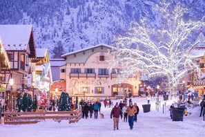A snow-covered town square with buildings and a large tree decorated with lights.