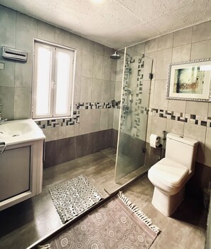 Ein Badezimmer mit Dusche, Toilette, Waschbecken und einem Fenster.