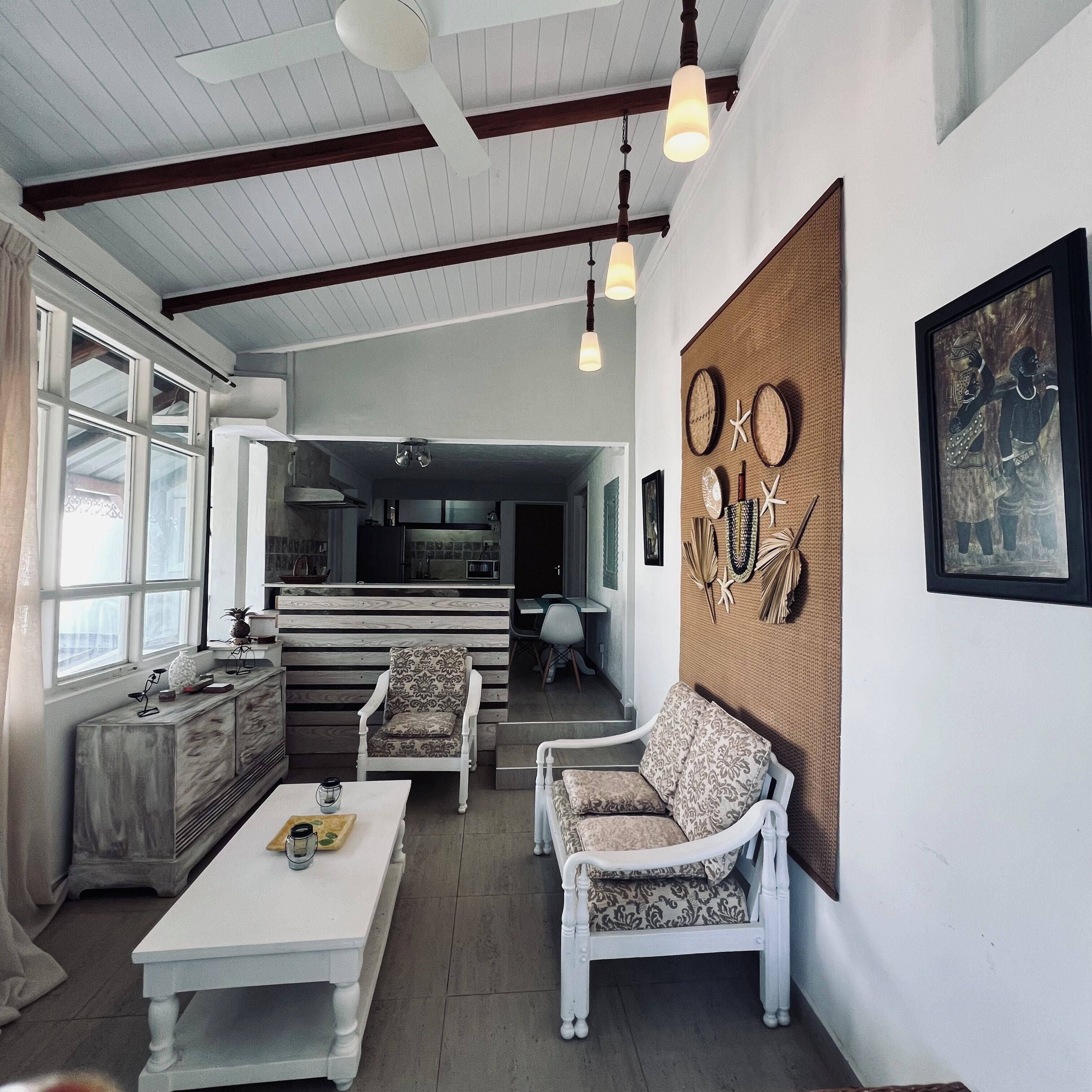 A spacious living area with a high ceiling, a dining table, two white armchairs, and a kitchen in the background.