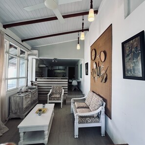 Een ruime woonkamer met een hoge plafond, een eettafel, twee witte fauteuils en een keuken op de achtergrond.