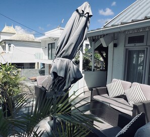 An outdoor seating area with a covered umbrella, a wicker sofa, and a potted plant. - Stylish couples Beach Escape in Pointe aux Canonniers (Pointe aux Canonniers)
