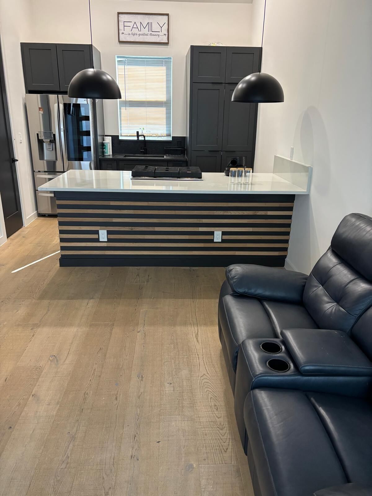 A modern kitchen with a central island, black cabinets, and a black leather couch.