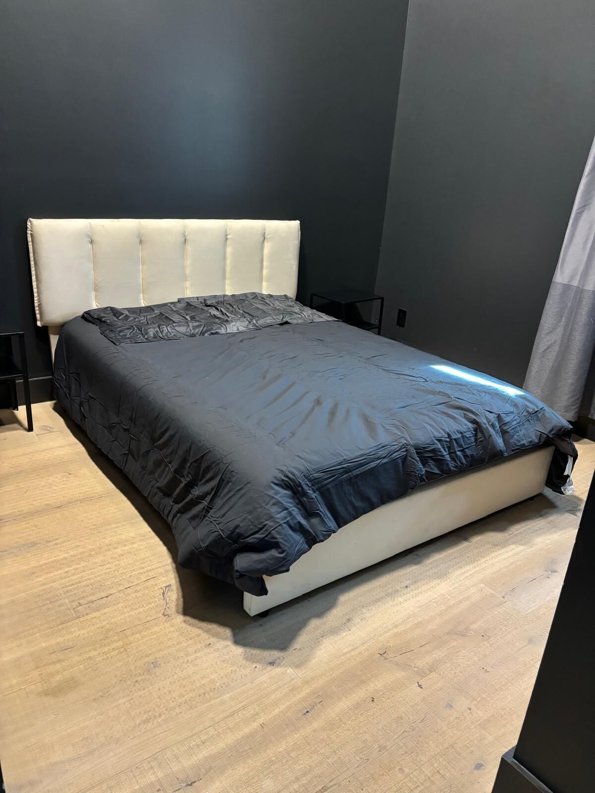 Una cama con cabecera, colchón oscuro y suelo de madera.