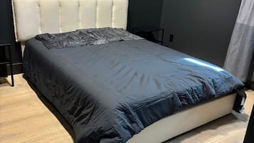 Una cama con cabecera, colchón oscuro y suelo de madera.
