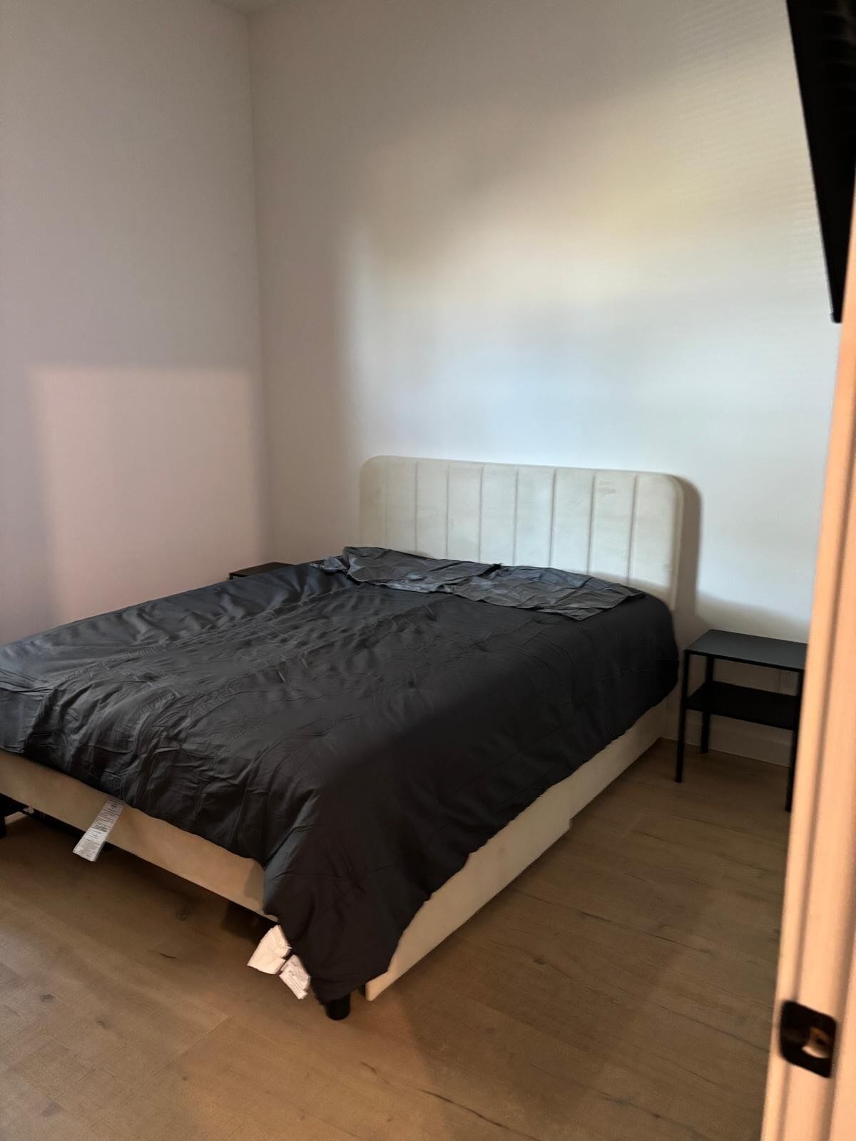 Una cama individual con cabecera blanca en una habitación con paredes de tonos claros y suelo de madera.